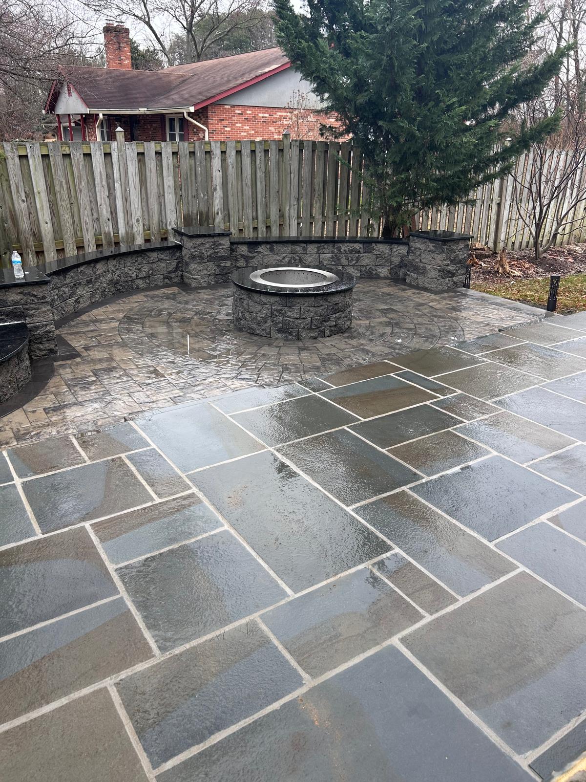 Stone fire-pit patio with seat walls under bare winter trees by Kaeler